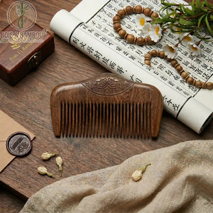 Peigne de poche en bois de santal sculpté avec motifs floraux. Posé sur une table en bois avec décor zen, calligraphie et perles. Accessoire de coiffure naturel et artisanal.