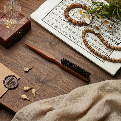 Peigne moelleux en poils de sanglier naturels avec manche en bois pointu. Posé sur une table avec calligraphie, perles et fleurs. Brosse de coiffage pour volume et finition précise.