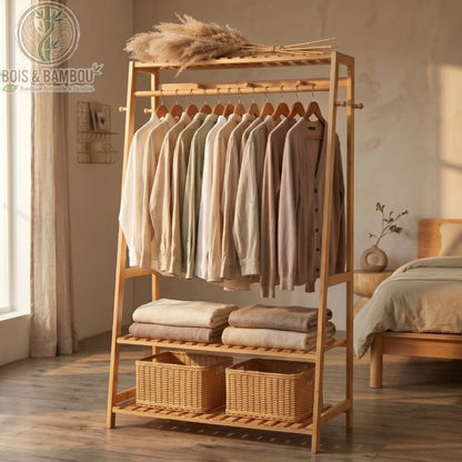 Penderie Bambou Naturel avec etageres et Crochets situation. Un portant en bois clair avec vêtements suspendus, piles de linge et paniers en osier, dans une chambre minimaliste baignée de soleil.