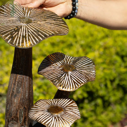 Champignon en bois décoratif finition bois naturel tenu à la main, gros plan sur les stries dorées
