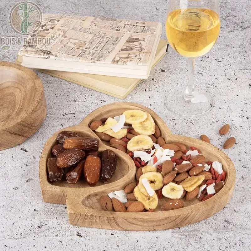 Plateau Double Cœur en Bois de Manguier. Un plateau artisanal avec deux compartiments, l'un pour les dattes, l'autre pour le mélange de noix, banane et noix de coco, à côté de vin.