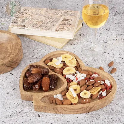 Plateau Double Cœur en Bois de Manguier. Un plateau artisanal avec deux compartiments, l'un pour les dattes, l'autre pour le mélange de noix, banane et noix de coco, à côté de vin.