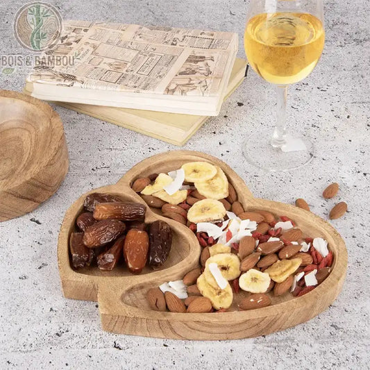 Plateau Double Cœur en Bois de Manguier. Un plateau artisanal avec deux compartiments, l'un pour les dattes, l'autre pour le mélange de noix, banane et noix de coco, à côté de vin.