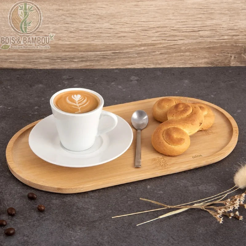 Plateau Ovale en Bambou. Un plateau ovale en bambou clair présentant une tasse de café au lait avec latte art, une cuillère et des petits pains dorés sur une surface sombre.