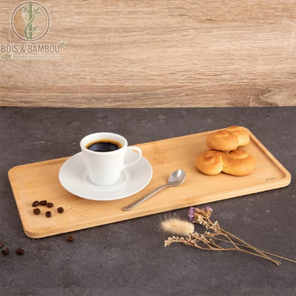 Plateau Rectangulaire en Bambou. Un long plateau en bambou clair portant une tasse de café blanc, une cuillère, des petits pains dorés et des fleurs séchées sur un fond sombre.