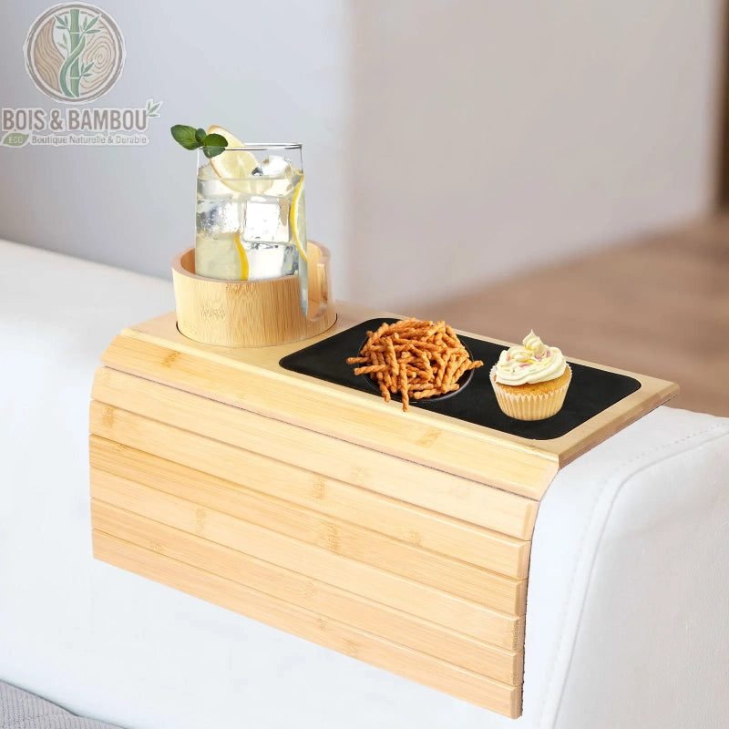 Plateau d accoudoir de canape en bambou 6. Plateau flexible en bambou clair sur un canapé blanc, comprenant un porte-gobelet avec un verre citronné, des biscuits salés et un cupcake sur un tapis noir.