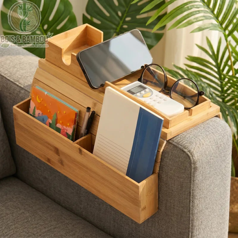 Plateau d accoudoir de canape en bambou 8. Un plateau organisateur flexible en bambou sur un canapé gris, avec des compartiments contenant un smartphone, des lunettes, une télécommande et des carnets.