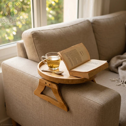Plateau d accoudoir de canape en bambou rond situation 2. Un plateau circulaire en bambou clipsé sur l'accoudoir d'un canapé gris, supportant une tasse de thé et un livre ouvert pour un moment cocooning.