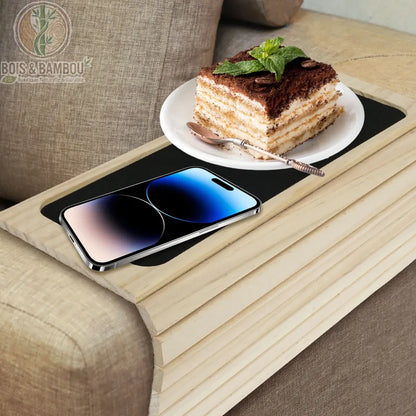 Plateau d'accoudoir de canapé en bambou. Un plateau flexible en bois clair épousant la forme de l'accoudoir, avec une surface antidérapante supportant un téléphone et un gâteau.