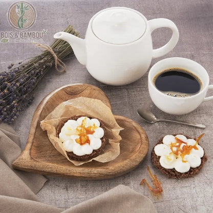 Plateau en Bois de Manguier Cœur. Petit plateau artisanal en forme de cœur avec une pâtisserie, accompagné d'une théière blanche, d'un café et d'un bouquet de lavande séchée.