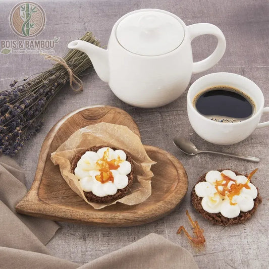 Plateau en Bois de Manguier Cœur. Petit plateau artisanal en forme de cœur avec une pâtisserie, accompagné d'une théière blanche, d'un café et d'un bouquet de lavande séchée.