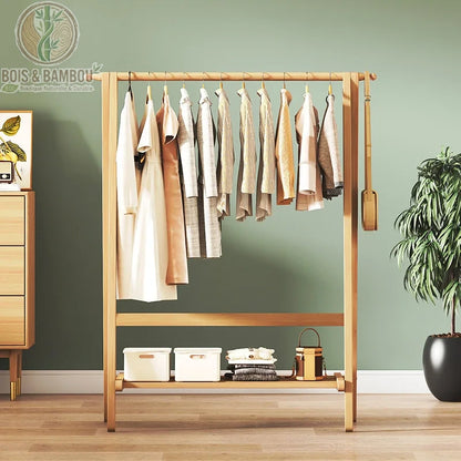 Portant à Vêtements en Bambou. Un penderie élégante en bois clair avec une longue tringle chargée de vêtements et une étagère basse pour boîtes et sacs devant un mur vert sauge.