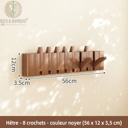 Porte Manteau Piano hetre fonce 8 crochets. Un porte-manteau mural de 56 cm en bois de hêtre couleur noyer avec 8 crochets rabattables, affichant ses dimensions sur un mur ensoleillé.