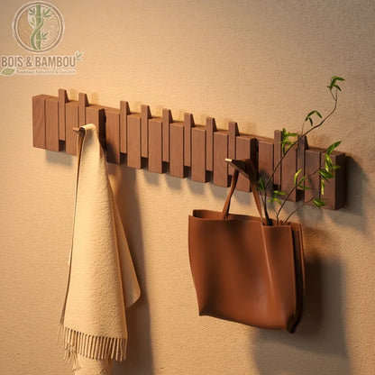 Porte-Manteau Piano. Un support mural original en bois aux crochets rabattables semblables à des touches de piano, supportant une écharpe beige et un sac à main marron.