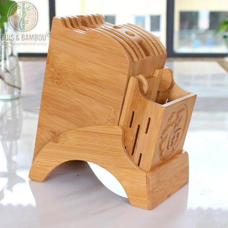 Porte-couteau de cuisine en bambou. Un bloc de rangement robuste en bambou avec plusieurs fentes pour couteaux et un compartiment gravé, posé sur un plan de travail blanc.