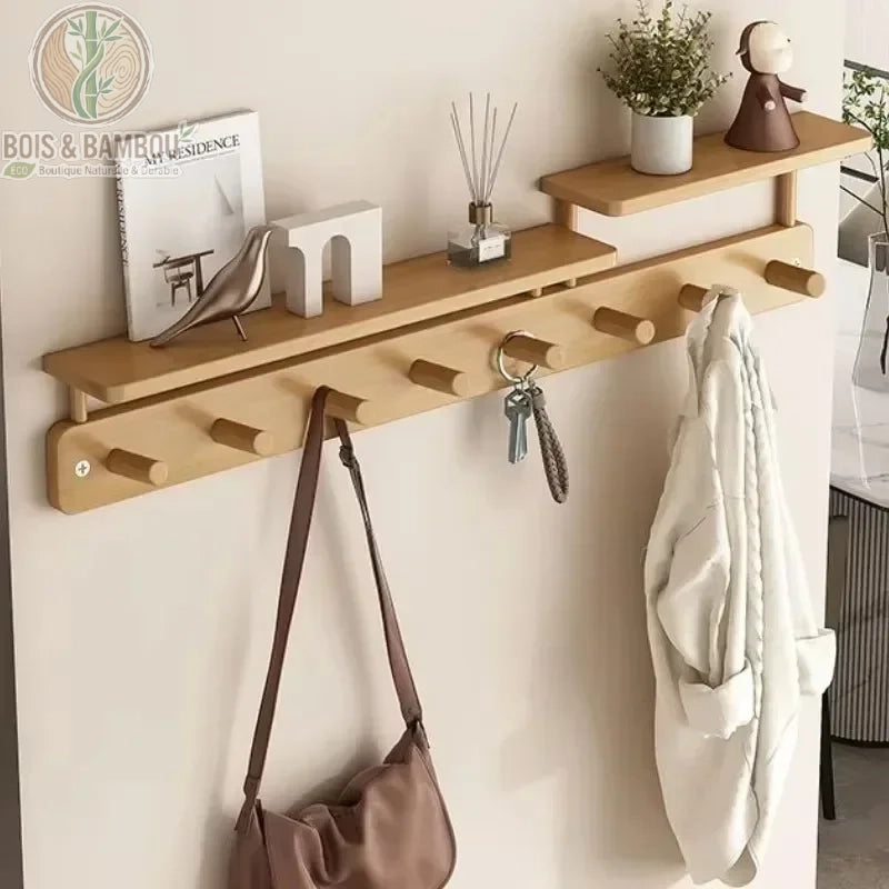 Porte-manteau mural créatif en bambou. Un support mural en bois clair avec plusieurs patères cylindriques et deux tablettes décalées décorées, supportant un sac, des clés et une veste.