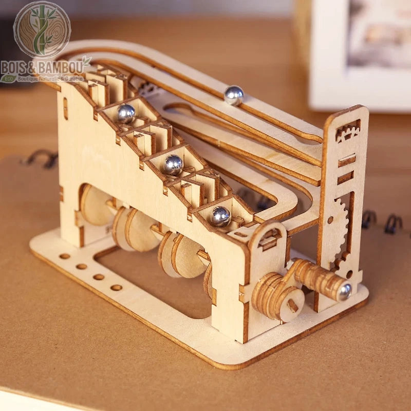 Puzzle 3D en bois Spirale Mécanique. Une petite machine manuelle en bois découpé permettant de faire monter des billes d'acier le long d'un escalier mécanique avant de redescendre.