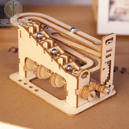 Puzzle 3D en bois Spirale Mécanique. Une petite machine manuelle en bois découpé permettant de faire monter des billes d'acier le long d'un escalier mécanique avant de redescendre.
