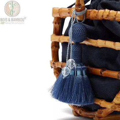 Sac corbeille en bambou a pompon details. Gros plan sur un pompon bleu à franges et perles décoratives, accroché à la structure d'un sac artisanal en tiges de bambou avec pochon noir.