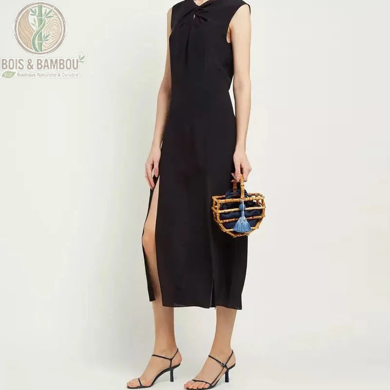 Sac corbeille en bambou a pompon situation 1. Une femme en robe noire élégante porte un petit sac corbeille en bambou avec un pochon bleu marine et un pompon assorti, pour un look chic et naturel.