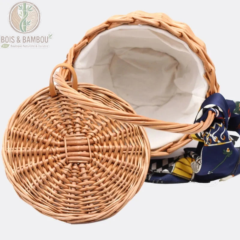 Sac panier en bambou et paille vue 2. Vue plongeante d'un panier seau en osier ouvert révélant une doublure en tissu blanc immaculé, avec son couvercle tressé assorti et un foulard décoratif bleu.