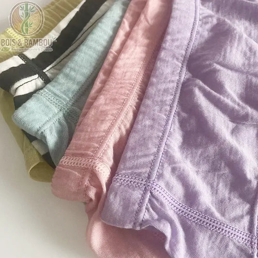 Slip bikini en laine mérinos et fibre de bambou. Gros plan sur une pile de sous-vêtements aux couleurs pastel (mauve, rose, bleu, rayé noir et blanc, vert) montrant la texture douce.