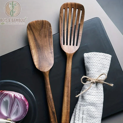 Spatule japonaise en bois naturel. Une spatule pleine et une spatule ajourée en bois sombre texturé, posées sur une plaque noire avec un oignon rouge et un torchon noué.