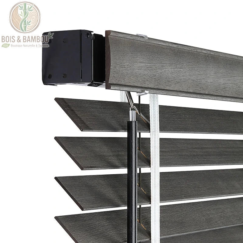 Vue détaillée du mécanisme supérieur de stores vénitiens en bois de tilleul gris foncé sur mesure. Boîtier de commande noir, tige et corde de levage. Lamelles texturées avec grain de bois.