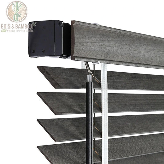 Vue détaillée du mécanisme supérieur de stores vénitiens en bois de tilleul gris foncé sur mesure. Boîtier de commande noir, tige et corde de levage. Lamelles texturées avec grain de bois.