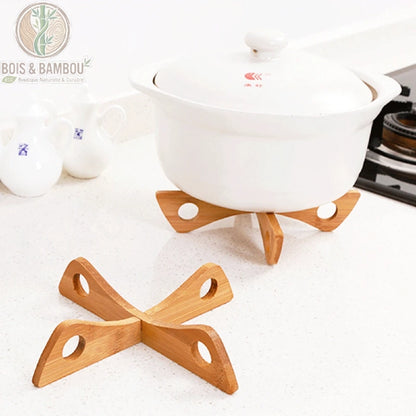 Support de Pot Croisé en Bambou. Deux dessous-de-plat en bambou en forme de croix avec des perforations circulaires, l'un soutenant une cocotte blanche sur un plan de travail clair.