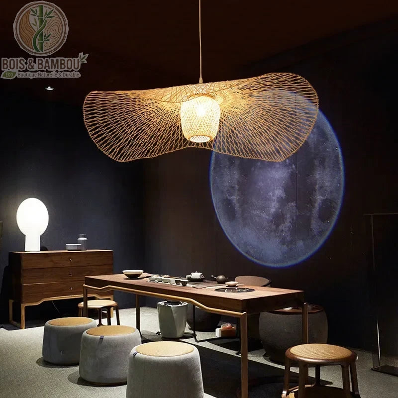 Suspension en bambou au design aérien et ondulé, rappelant la légèreté d'un chapeau de paille traditionnel. Son tressage artisanal complexe et sa structure évasée diffusent une lumière douce tout en créant un point focal artistique.