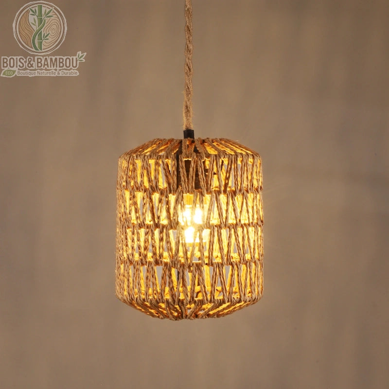 Suspension en rotin naturel tressé , un luminaire cylindrique artisanal avec un tressage ajouré laissant passer une lumière tamisée, suspendu par une corde en jute assortie.