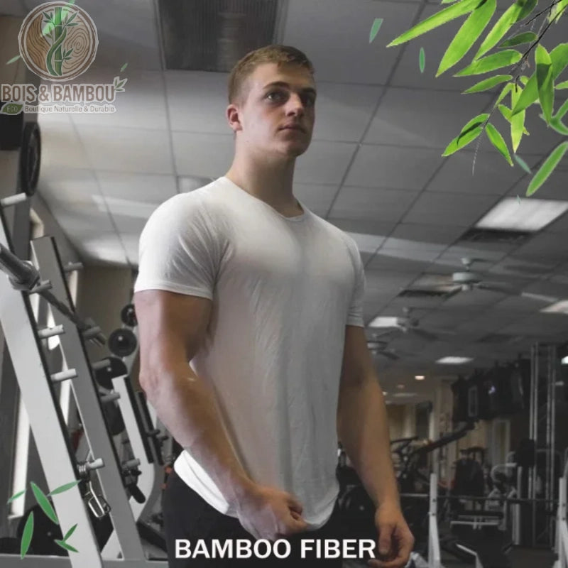 T-shirt sport et détente en fibre de bambou. Un homme musclé porte un t-shirt blanc moulant en fibre de bambou, se tenant debout dans une salle de sport remplie d'équipements de musculation.