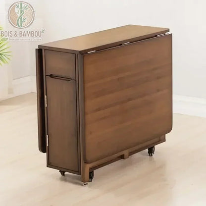 Table a manger pliante en bambou marron repliee. Table en bambou marron foncé totalement repliée sur roulettes, illustrant un design compact et un gain de place optimal pour les petits espaces.