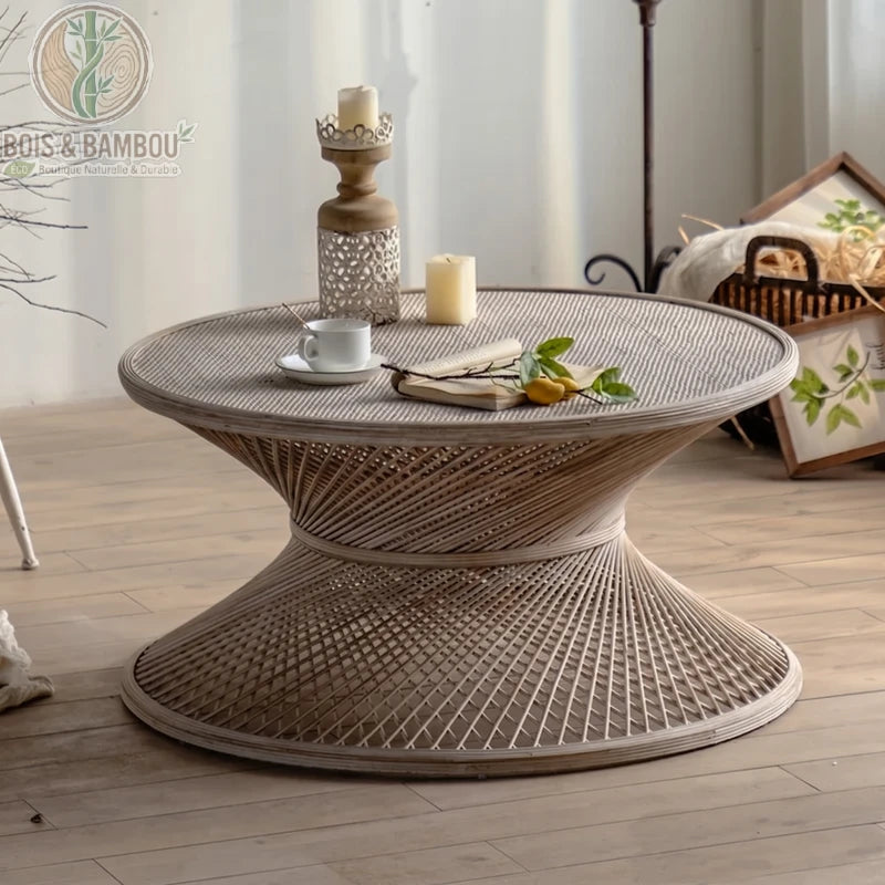 Table basse ronde en rotin et bambou grand . Zoom sur une table basse circulaire en rotin tressé au design en sablier, accueillant une tasse de café, un livre et des bougies dans un cadre serein.