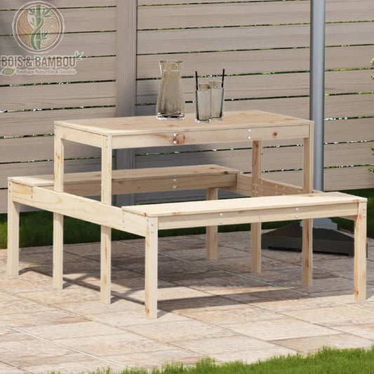 Table de Pique-nique en Pin. Un ensemble de jardin en pin clair composé d'une table rectangulaire et de deux bancs intégrés, installé sur une terrasse en dalles devant une clôture.