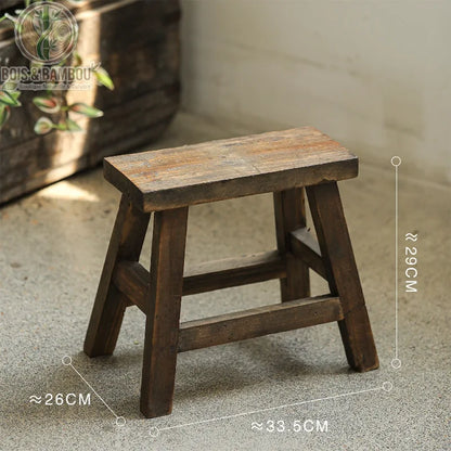 Tabouret bas en bois grand. Schéma technique d'un tabouret rustique en bois foncé de taille moyenne, indiquant ses mesures : environ 33,5 cm de long, 29 cm de hauteur et 26 cm de profondeur.