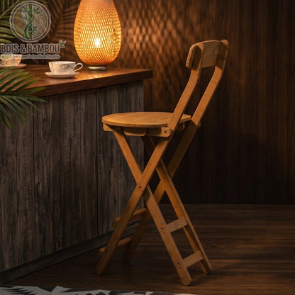 Tabouret de Bar en Bambou situation 3. Tabouret pliant en bambou placé devant un comptoir en bois sombre, éclairé par une lampe d'ambiance chaleureuse pour une atmosphère cosy et naturelle.