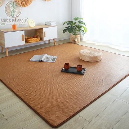 Tapis Tatami en Rotin, un grand tapis rectangulaire en fibres naturelles tressées posé sur un parquet clair, agrémenté d'un coussin de sol en paille et d'un plateau à thé, créant une atmosphère sereine et minimaliste dans une pièce lumineuse.