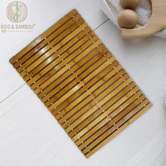 Tapis en bambou naturel artisanale pliable, composé de lattes horizontales en bois clair reliées de manière flexible. Sa structure ajourée assure une ventilation optimale et un séchage rapide, tandis que sa finition vernie souligne le grain naturel du bambou tout en offrant une résistance accrue à l'humidité.