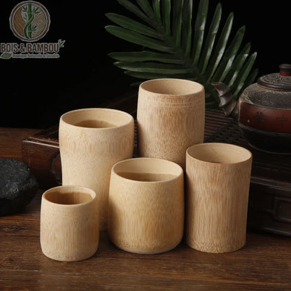 Tasse en bambou carbonisé rétro. Un ensemble de cinq tasses cylindriques en bambou de différentes tailles, disposées sur un plateau en bois sombre à côté d'une théière ancienne.