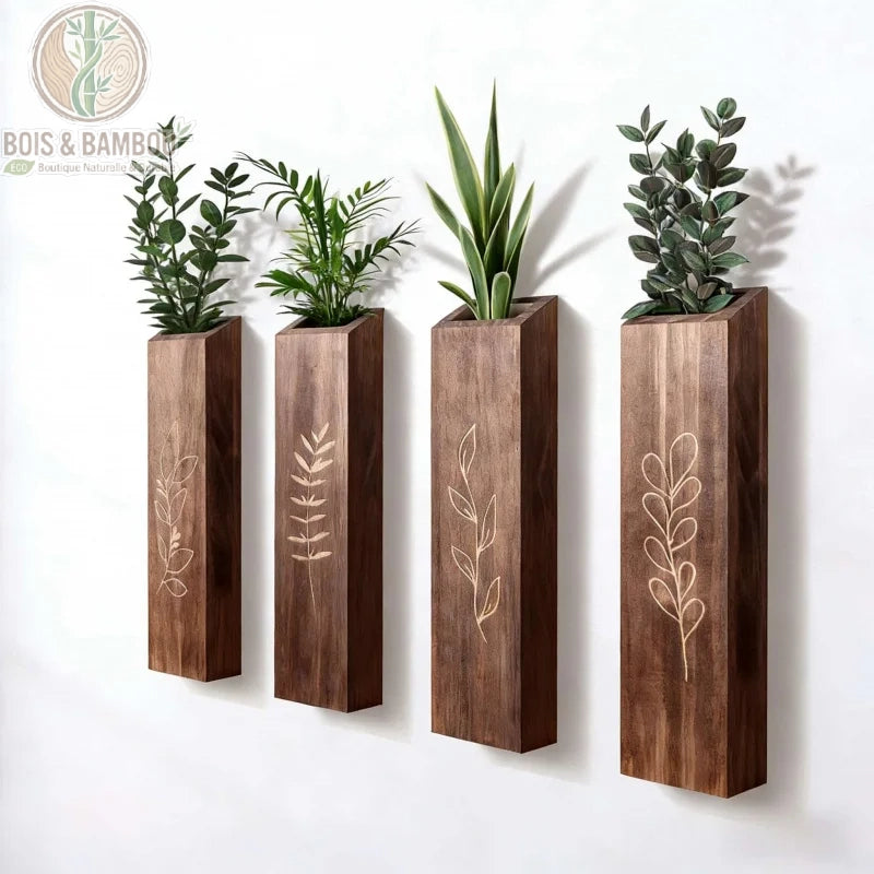 Vases Muraux en Bois. Quatre jardinières murales verticales en bois sombre avec des gravures de feuillage, alignées sur un mur blanc et contenant diverses petites plantes vertes.