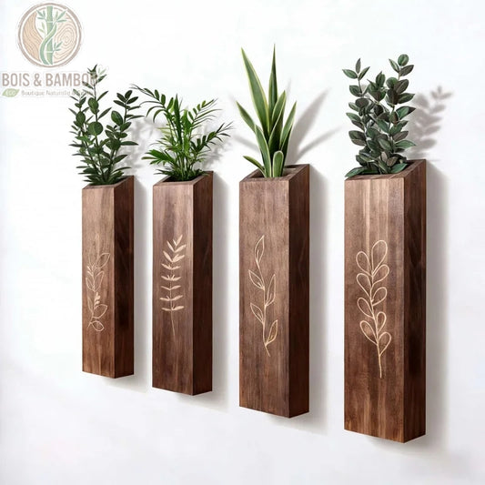 Vases Muraux en Bois. Quatre jardinières murales verticales en bois sombre avec des gravures de feuillage, alignées sur un mur blanc et contenant diverses petites plantes vertes.