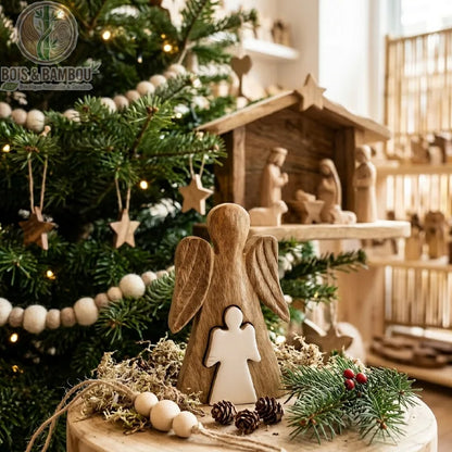Ange en bois de manguier émaillé blanc, posé près d'un sapin de Noël devant une crèche en bois