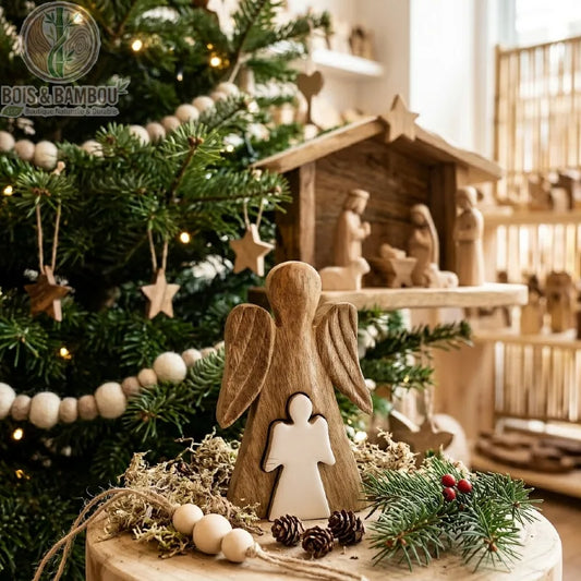 Ange en bois de manguier émaillé blanc, posé près d'un sapin de Noël devant une crèche en bois