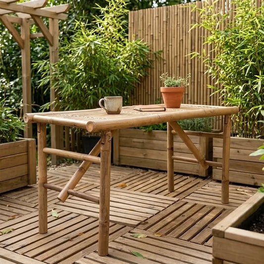Banc de jardin en bambou pliable utilisé en table basse sur une terrasse en bois, avec tasse, livre et pot d'aromates