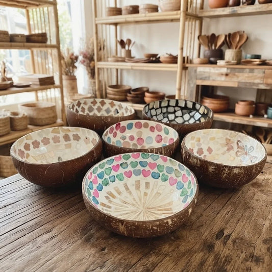 Six bols en noix de coco incrustés de coquillage aux motifs variés, posés sur une table en bois brut