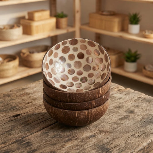 Pile de bols en noix de coco décoratifs à pastilles irisées sur fond blanc, posée sur une table en bois brut