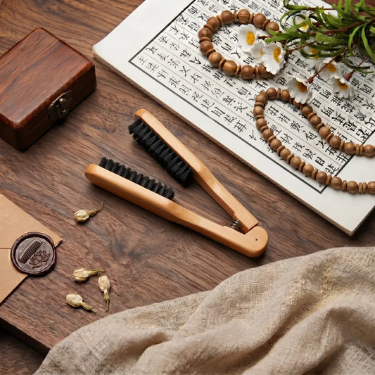 Brosse lissante à pince en bois avec poils de sanglier, double tête, posée sur un bureau en bois avec parchemin calligraphié et perles