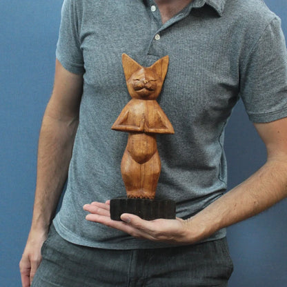 Chat en bois sculpté marron, posture yoga debout, tenu en main pour montrer sa taille compacte.